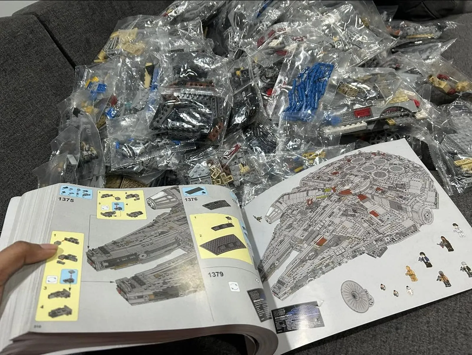 An open LEGO instruction manual at step 1,379 beside a sofa covered in bagged parts for a large spaceship build.